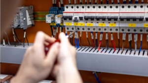 Elektryk precyzyjnie dokręca przewody w nowoczesnej rozdzielnicy elektrycznej za pomocą śrubokręta.